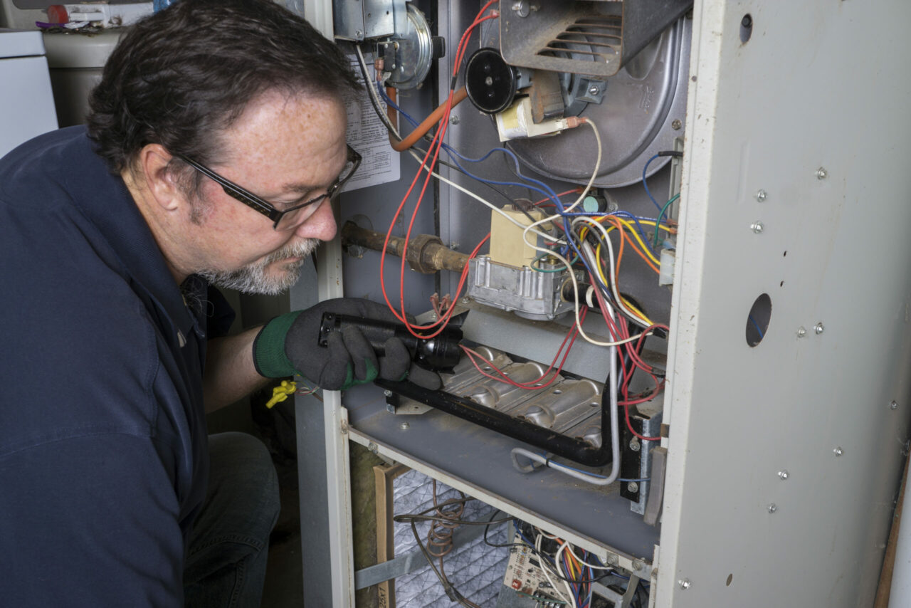 HVAC technician inspecting the control board of a gas furnace with a flashlight during troubleshooting