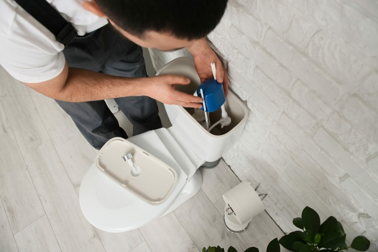 Male plumber replacing fill valve in toilet tank, closeup