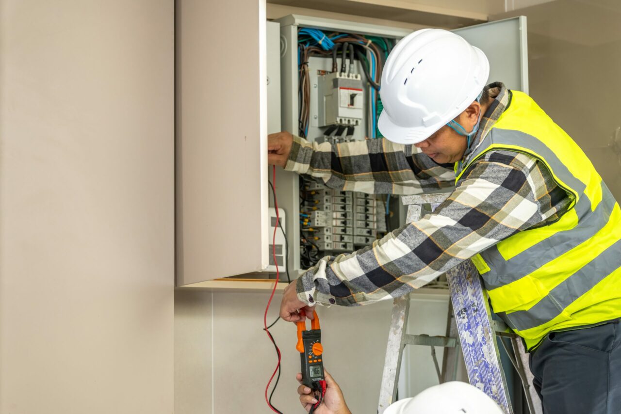 Skilled electrician worker inspecting electrical panel with multimeter testing wiring in residential building for safety and maintenance purposes.