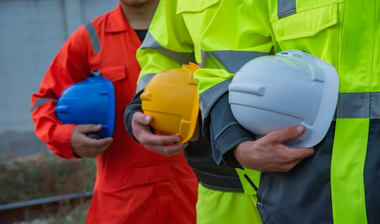 Construction workers in safety gear hold colorful hard hats