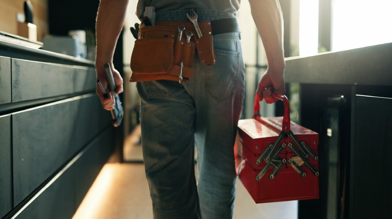 Person carrying a toolbox while walking through a home with tools on their belt.