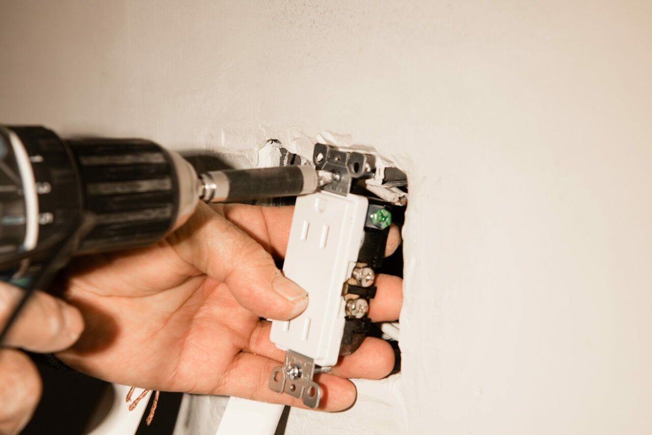 Electrician installing a duplex receptacle into an old-work box cut into an existing drywall wall