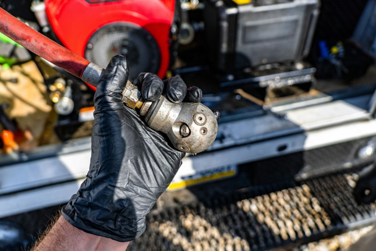 Plumber holding a jetter nozzle in front of a gas-powered sewer jetter unit