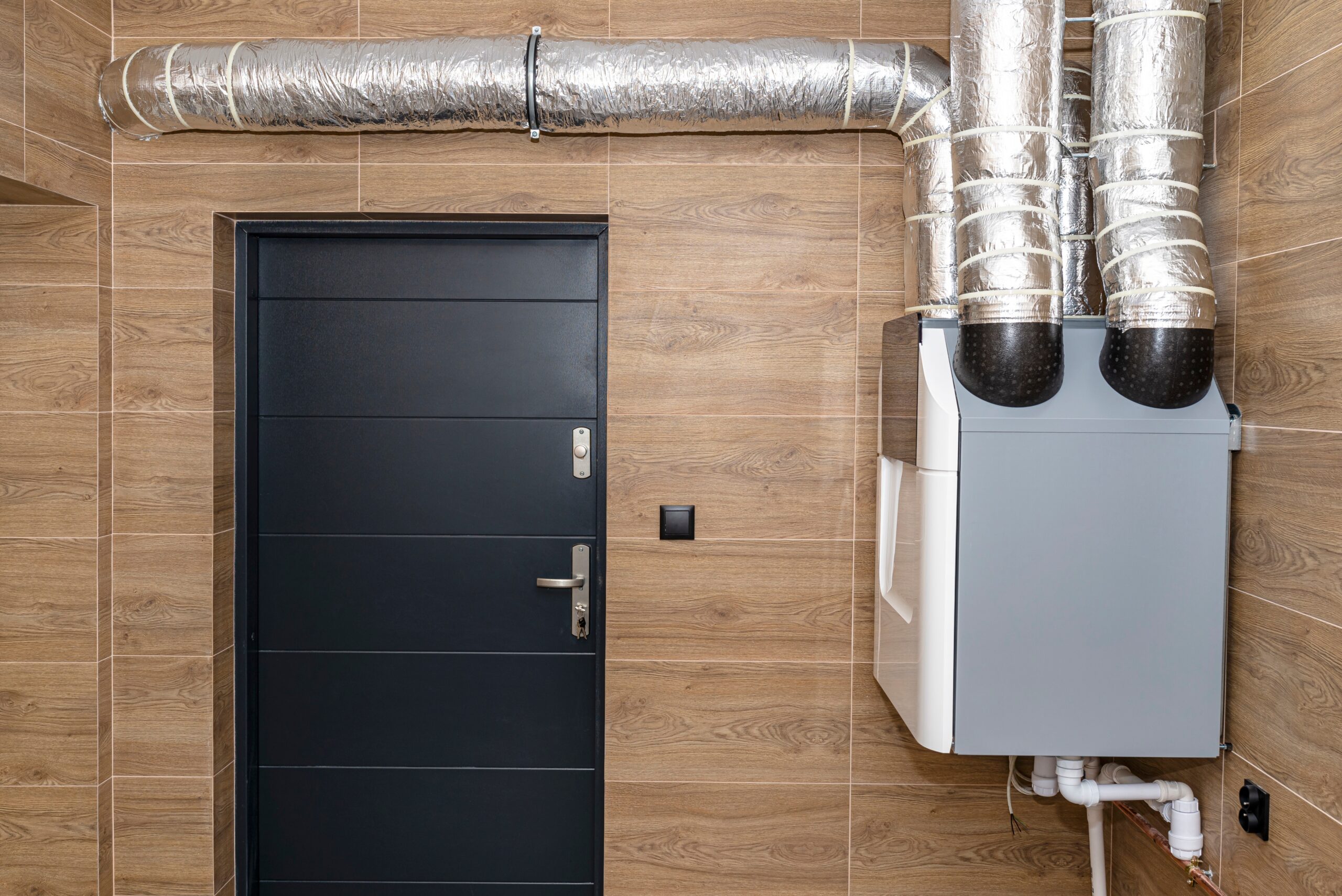 Heat recovery ventilator (HRV) wall unit with insulated ductwork in a residential utility room.