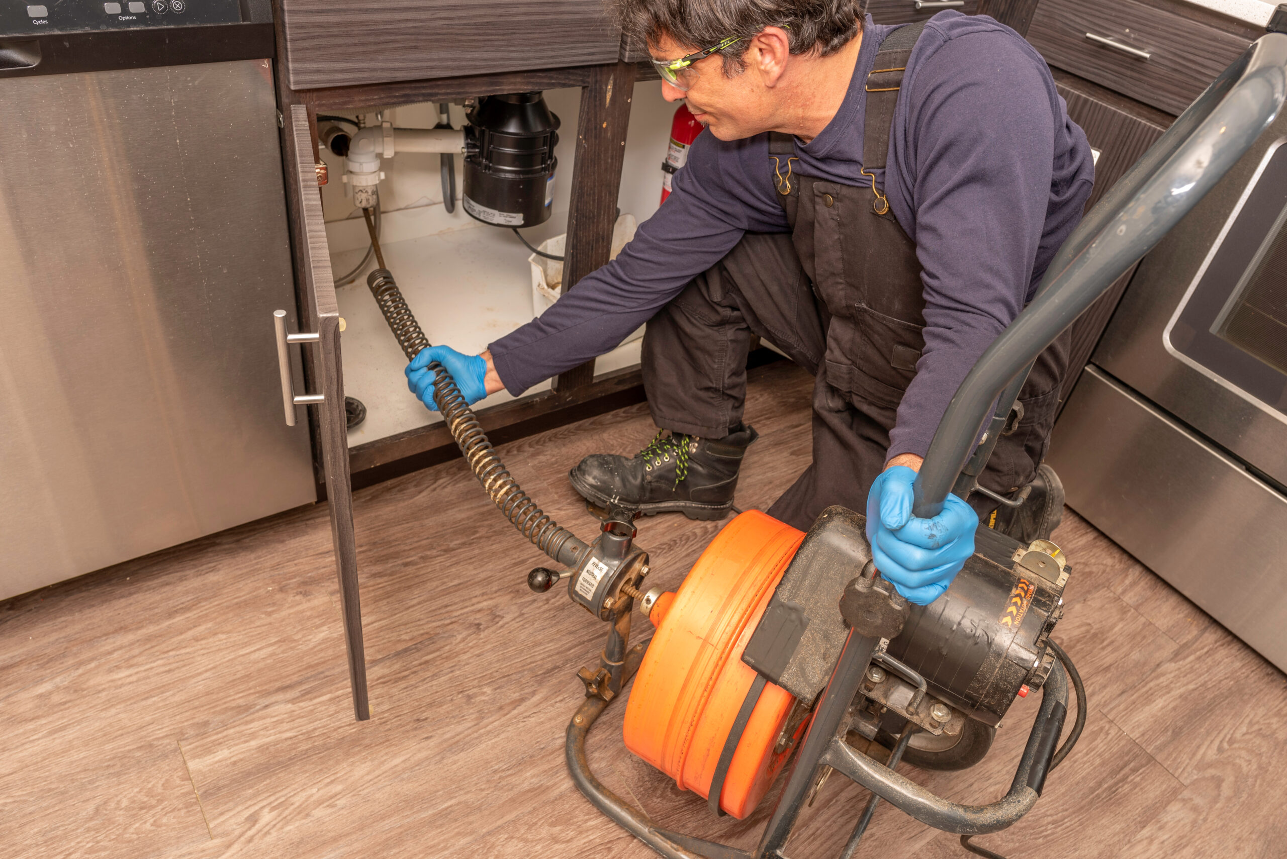 Plumber Using a Drum-Style Drain Cleaning Machine on a Kitchen Sink Line