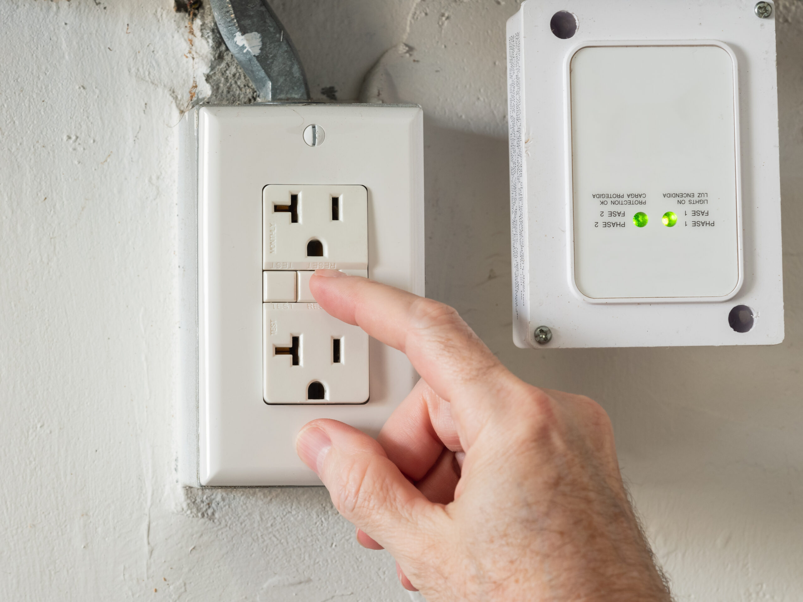 Close-up of a hand pressing the reset button on a residential GFCI outlet