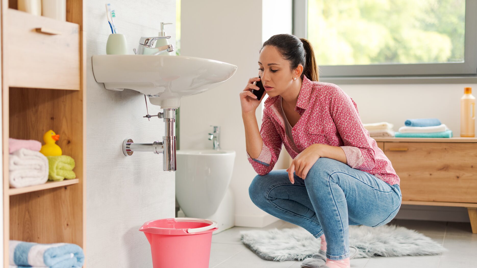 Homeowner inspecting a leaking pipe under a bathroom sink