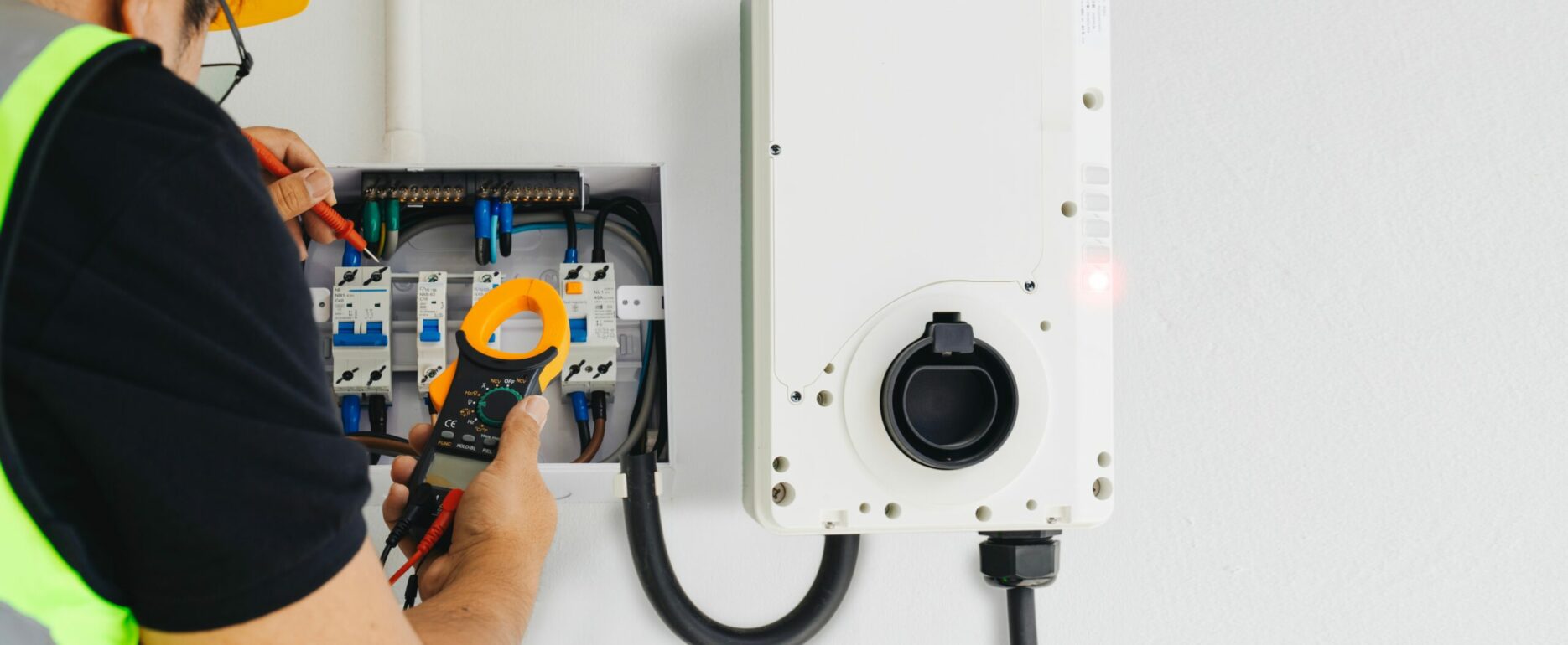 An electrician performing tests with a clamp meter during home EV charger installation.