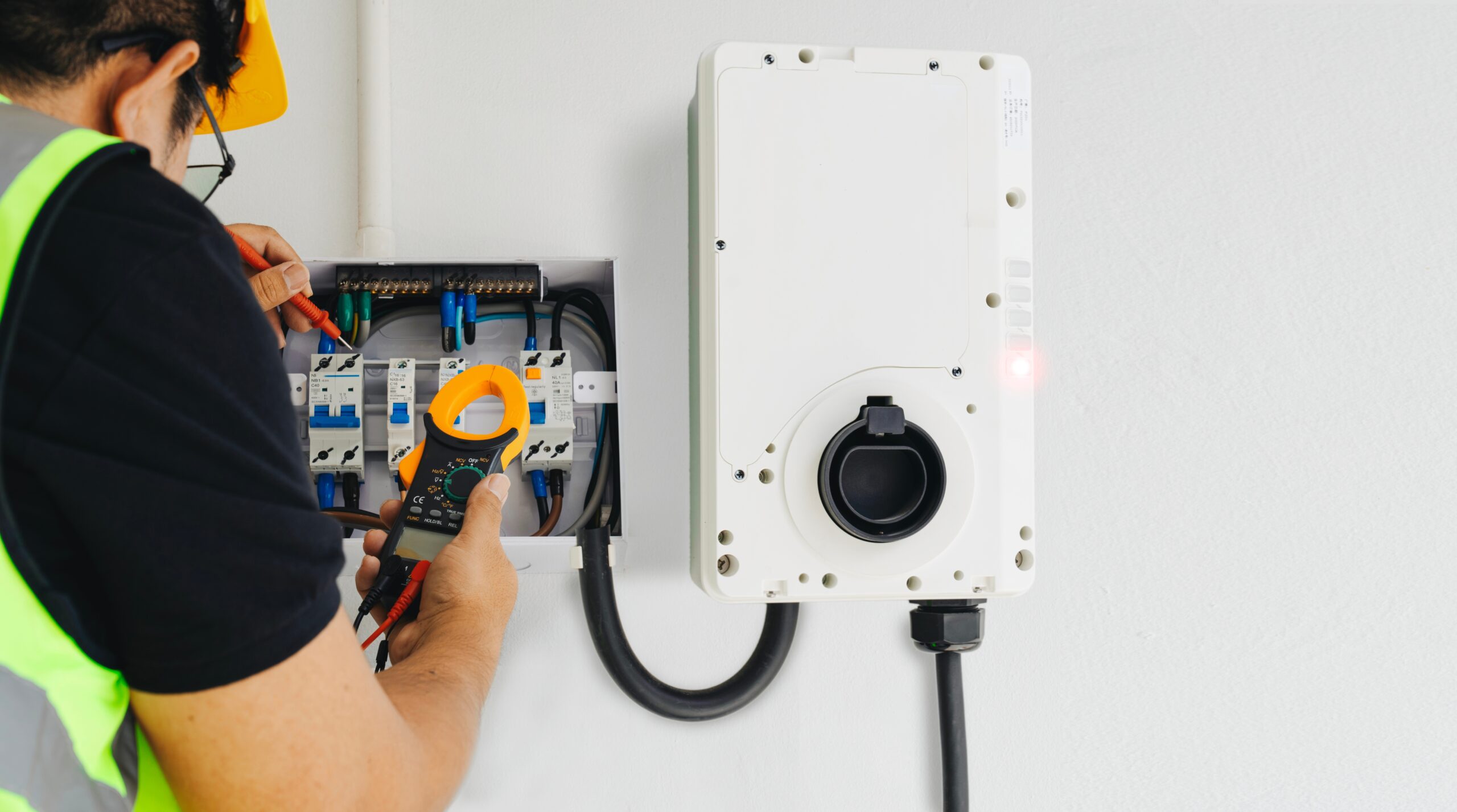 An electrician performing tests with a clamp meter during home EV charger installation.