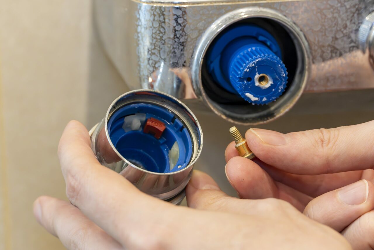 Hands removing shower mixer cartridge for bathroom faucet repair and replacement.