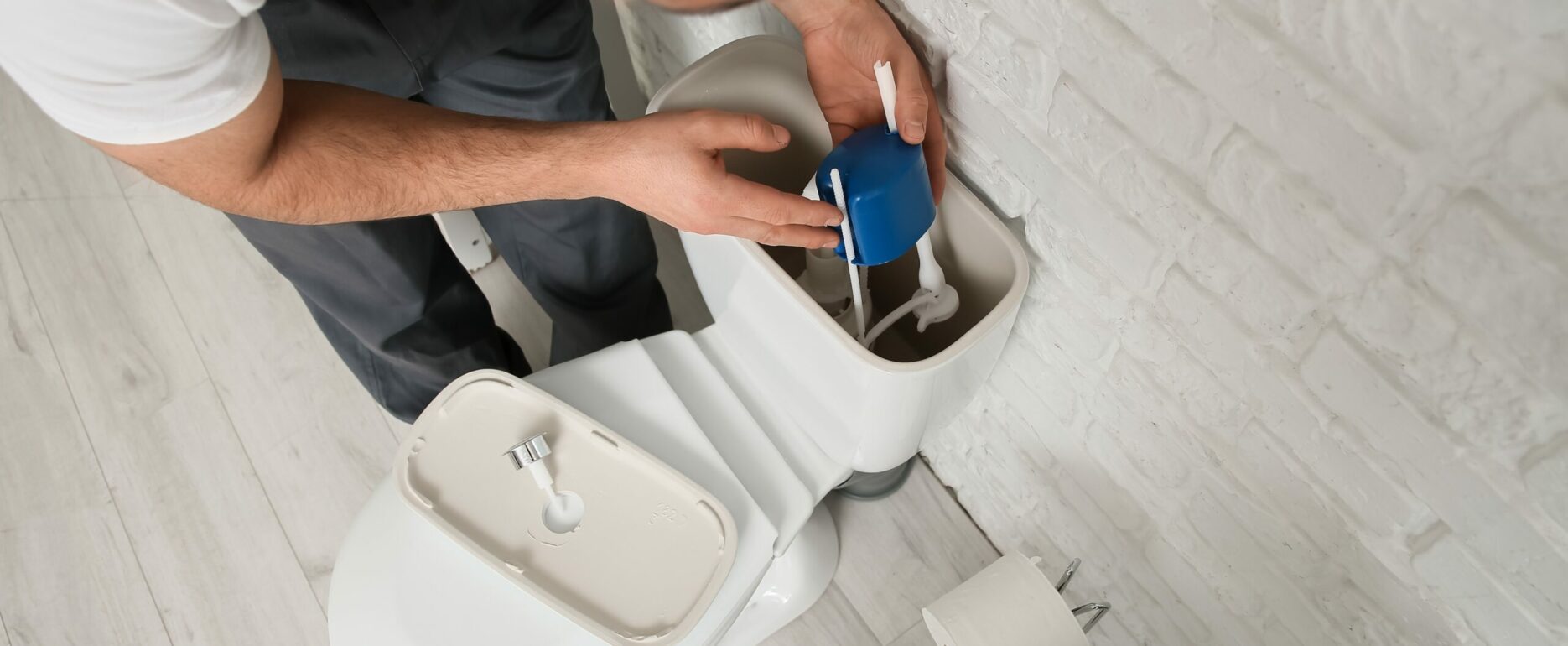 Male plumber replacing fill valve in toilet tank, closeup