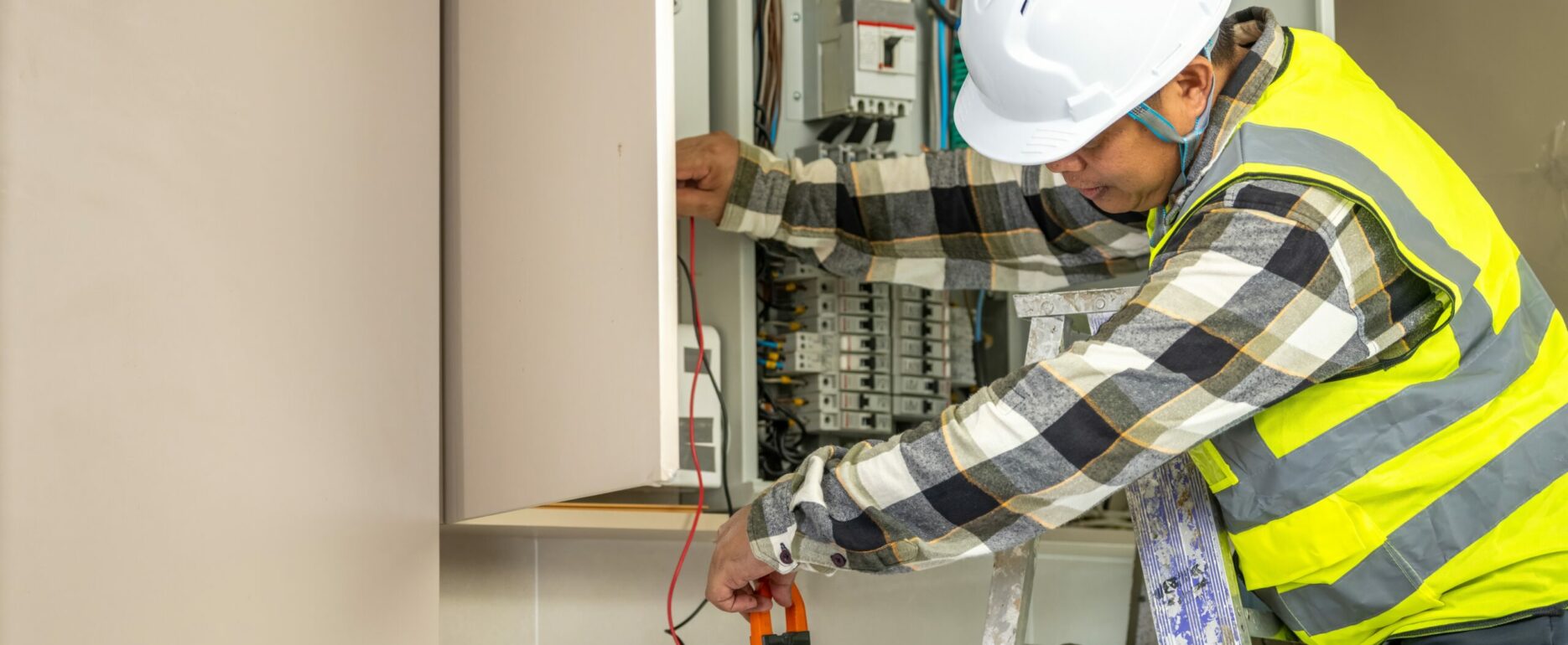 Skilled electrician worker inspecting electrical panel with multimeter testing wiring in residential building for safety and maintenance purposes.