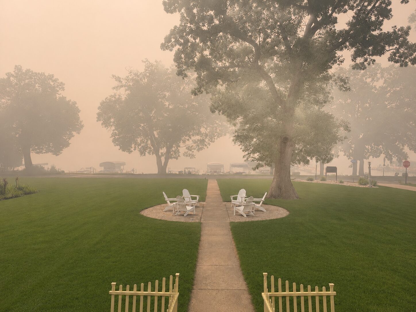 Wildfire smoke creating hazy conditions over a residential waterfront park with trees, lawn, and outdoor seating