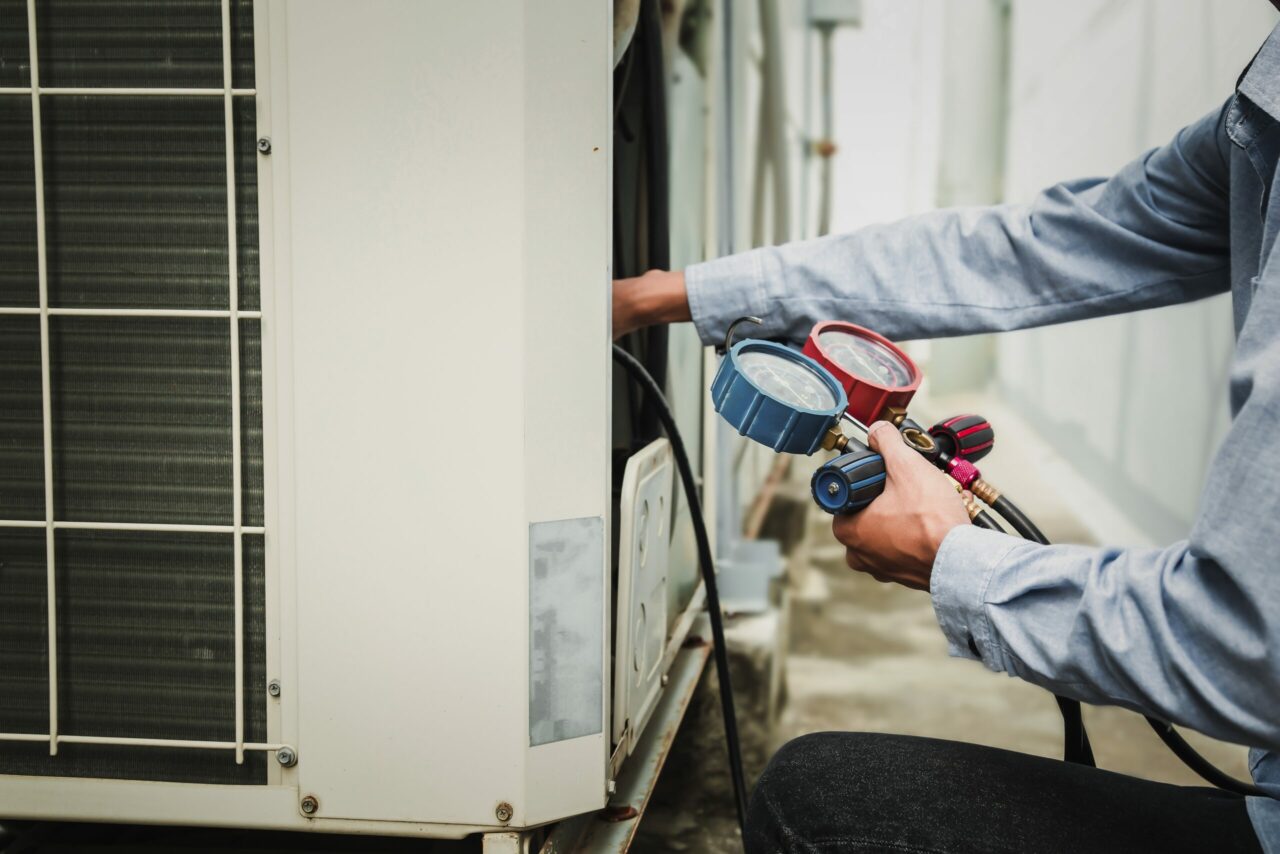 technician is using a manifold gauge to check the refrigerant in the system
