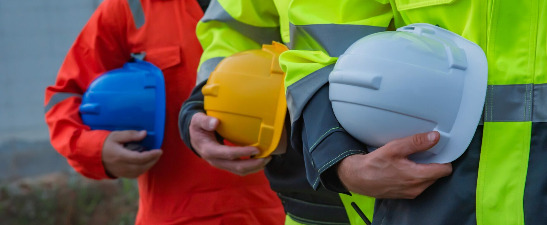 Construction workers in safety gear hold colorful hard hats