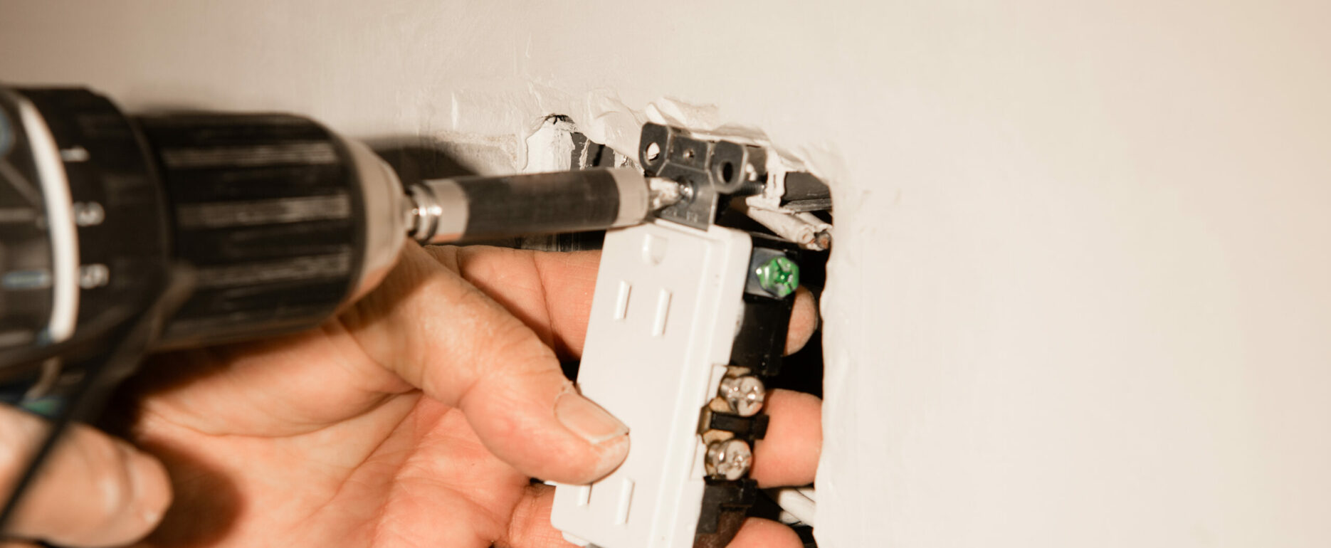 Electrician installing a duplex receptacle into an old-work box cut into an existing drywall wall