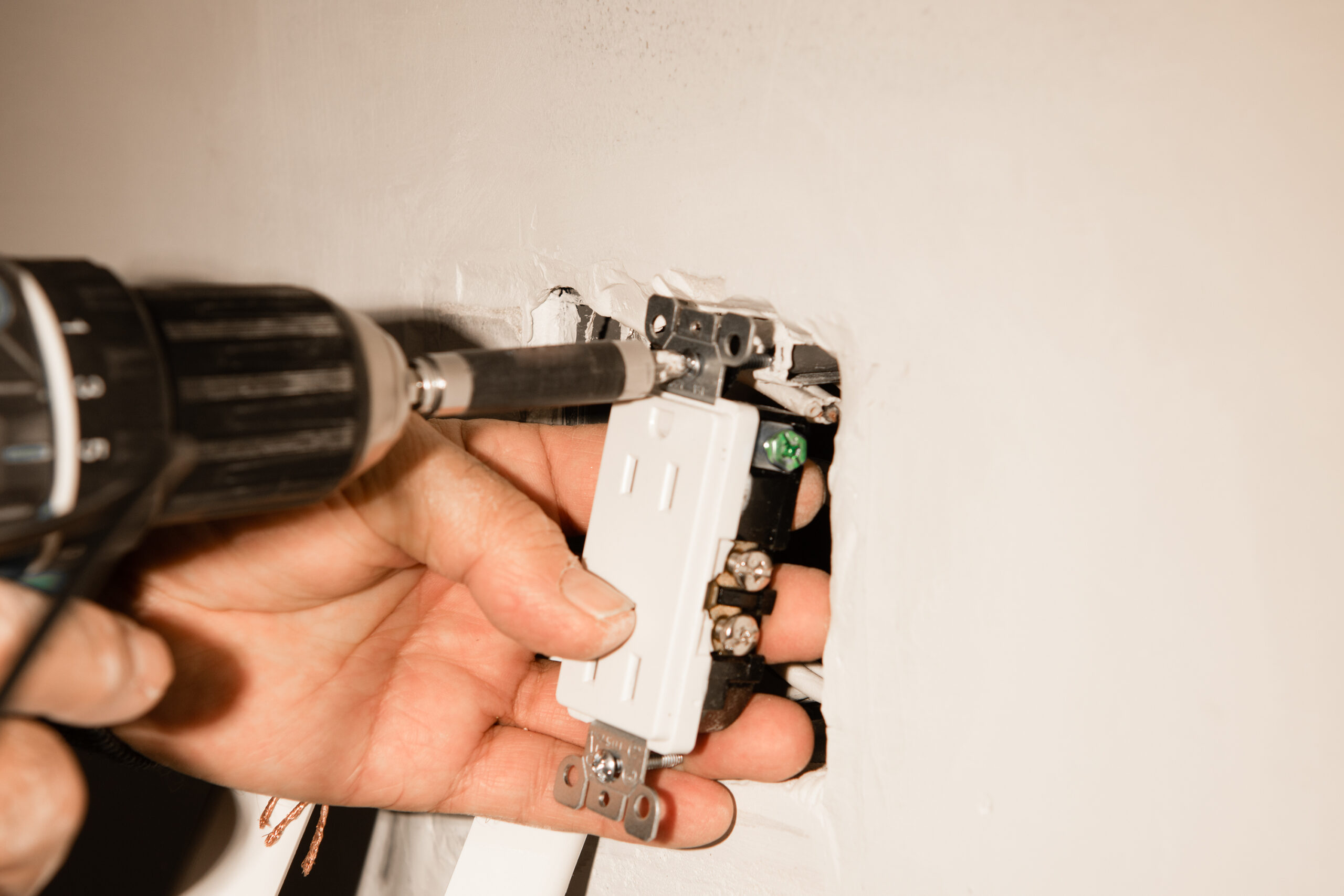 Electrician installing a duplex receptacle into an old-work box cut into an existing drywall wall