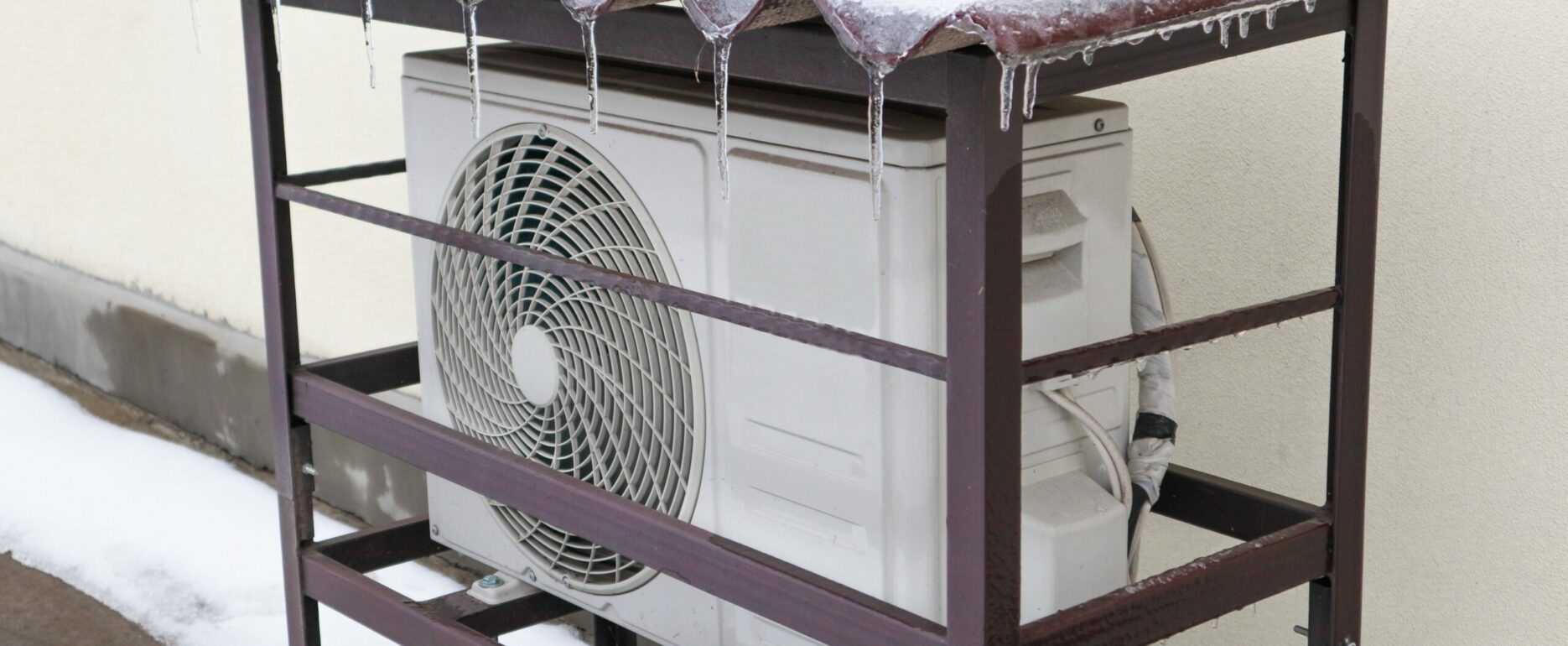 Heat pump mounted onto the wall of a house and covered in snow