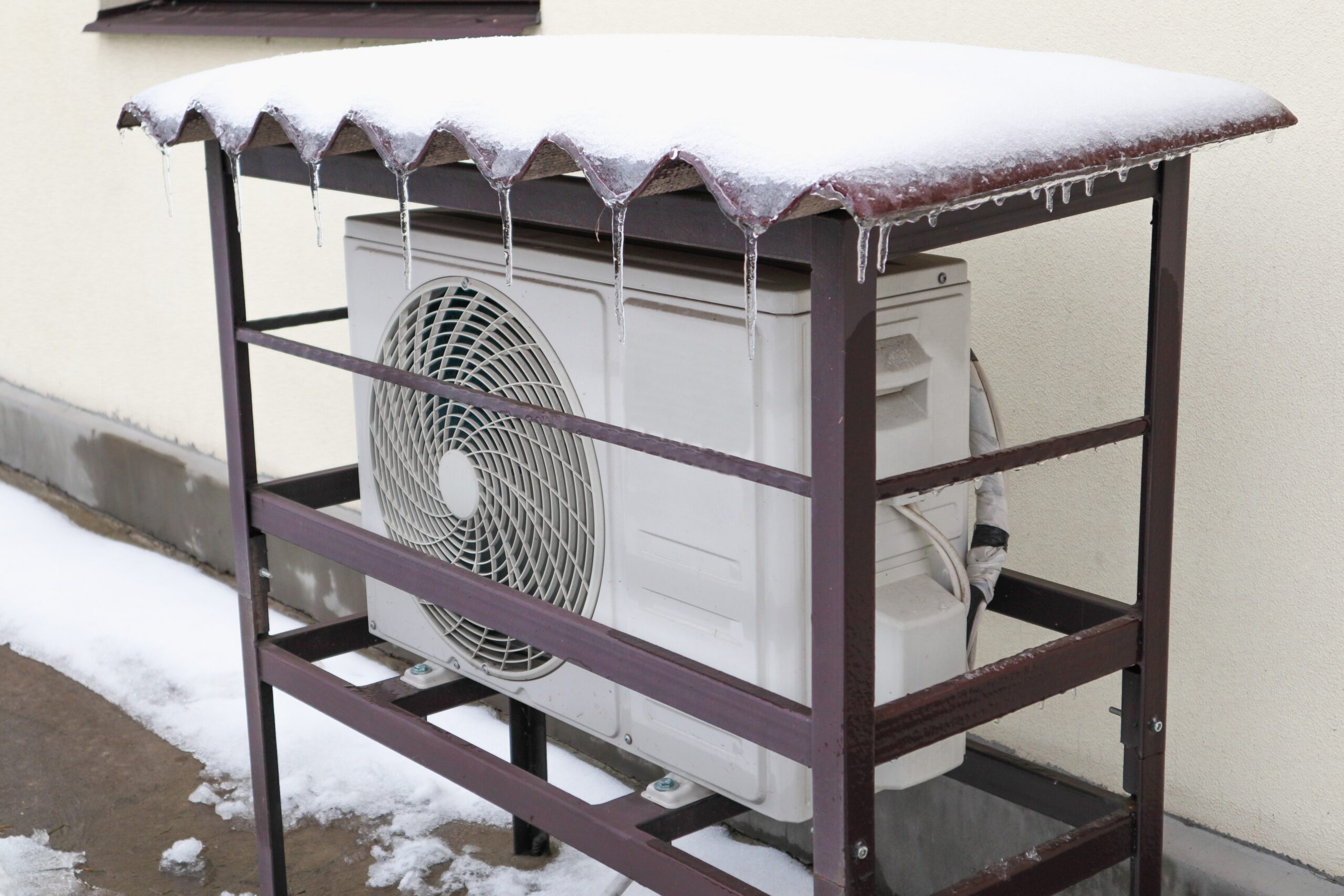 Heat pump mounted onto the wall of a house and covered in snow